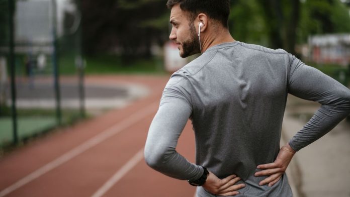 Exercising with sciatica: Image shows man in sports gear holding lower back