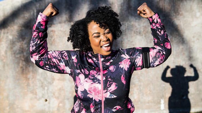 Woman in mauve zip up sports jacket with arms raised smiling