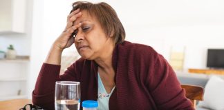 mature woman suffering from a migraine, head in her hand, with pills on the table next to a glass of water