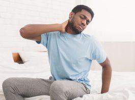 Man sat on the side of his bed holding his neck in pain