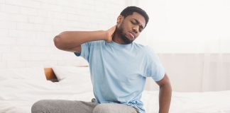 Man sat on the side of his bed holding his neck in pain