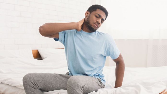 Man sat on the side of his bed holding his neck in pain