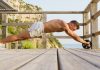 Image of man performing an ab wheel rollout without using knees outdoors by the ocean
