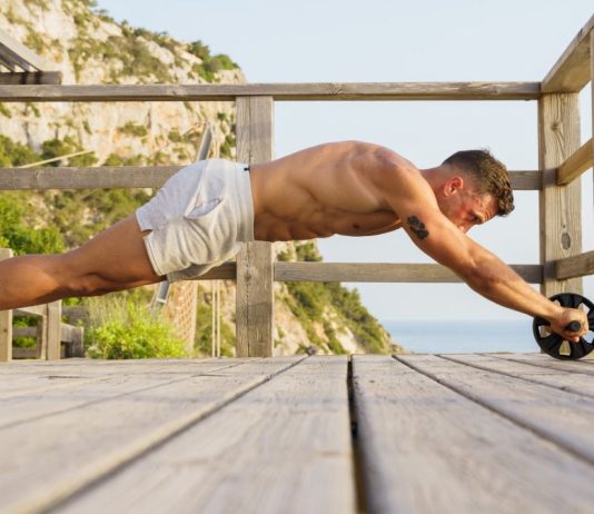 Image of man performing an ab wheel rollout without using knees outdoors by the ocean