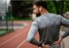 Sciatica: Man holding his lower back in pain during workout on a running track